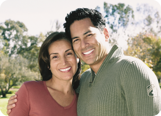 A happy couple smiling outdoors, showcasing bright and healthy teeth, representing the benefits of quality dental care.