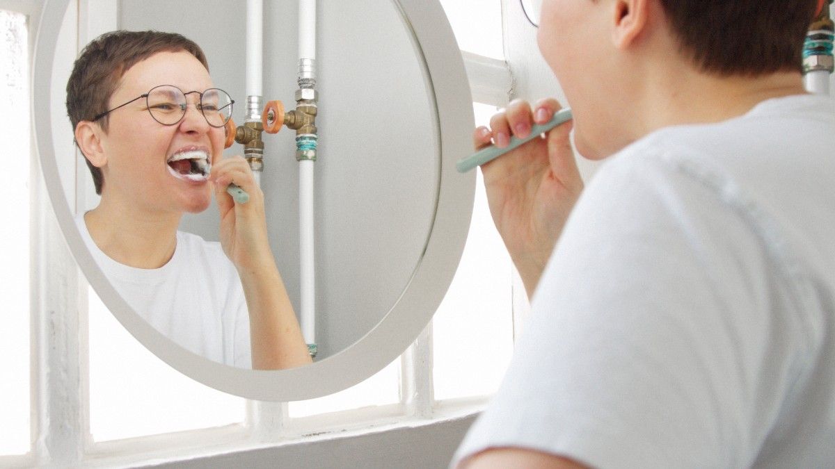 Person brushing teeth in front of mirror during daily oral care routine.