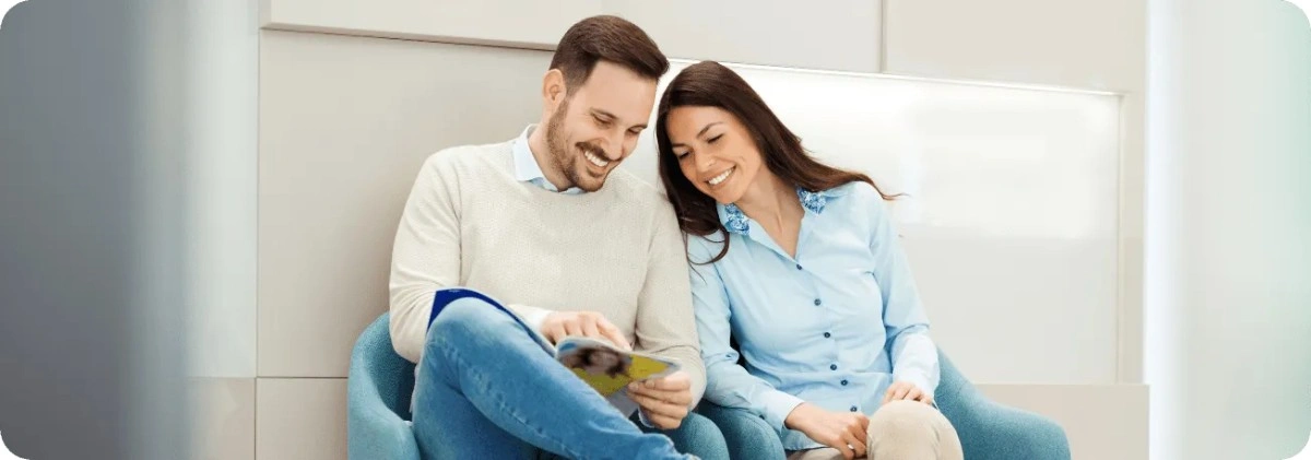 Couple smiling while reading magazine in dental waiting room.