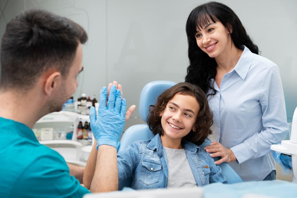 Child smiling at dentist and giving a high-five during dental visit with parent nearby